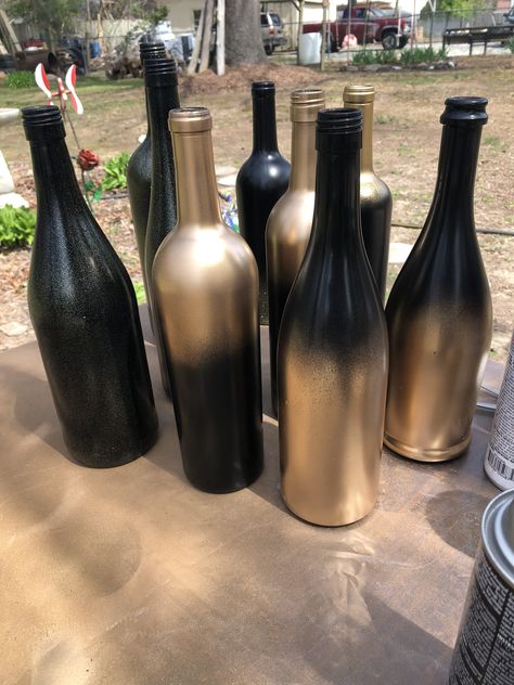 Black & gold wine bottle centerpieces Black And Gold Bottles Diy, Black And Gold Rustic Decor, Black Wine Bottle Decor, Diy Wine Bottle Centerpieces, Black And Gold Vase Centerpieces, Wine Bottle Centerpieces For Birthday, Black Gold Burgundy Wedding Centerpieces, Black And Gold Wine Bottle Centerpieces, Black And Gold Diy Decor