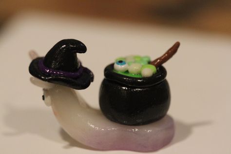 Handmade clay snail with cauldron on back. Snail has a purple hue on the bottom done with chalk pastel. The cauldron is bubbling over with green and glow in the dark stew and it seems an eye ball has risen to the top of the stew. Snail also features a witch hat. All pieces are handmade and my differ slightly from the picture. Halloween Clay Figures, Spooky Clay Ideas, Goth Clay Ideas, Clay Slugs, Cute Clay Stuff, Clay Cute Ideas, Little Clay Ideas, Clay Halloween Crafts, Tiny Clay Creations