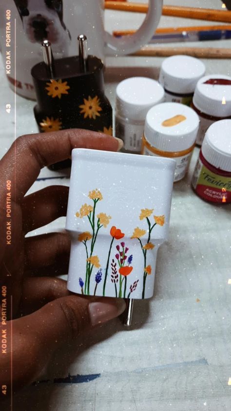 Flowers painted on a phone charger using acrylic paints. Charging Block Painting Ideas, Mobile Charger Painting, Painting On Charger, Phone Charger Painting Ideas, Paint Charger Cube, Charger Painting Ideas, Funky Crafts, Charger Art, Painted Things