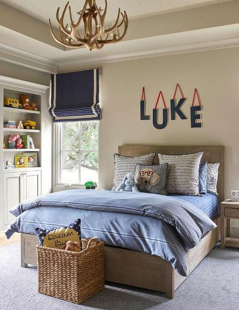 Blue wall letters hang from a cream colored wall above a light brown wood bed dressed in white and blue bedding flanked by light brown nightstands placed on a gray rug. Jenkins Interiors, Italian Cottage, Nightstand Design, Brown Nightstands, Boys Room Design, White Bedroom Decor, Blue Letters, Boy Bedroom Design, Wall Letters