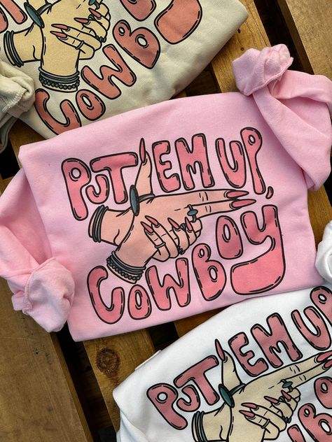 "Put Em Up, Cowboy" Sweatshirt Available in White, Pink & Cream Available in Crew Neck or Cut Out Neck Oversized & Slouchy Style ~ size down if you want it more fitted Super Soft 50% Cotton 50% Polyester Runs True Small 0/2/4 Medium 4/6/8 Large 8/10/12 XL 12/14/16 2XL 16/18/20 3XL 20/22/24 ***These Are PRINTED/MADE TO ORDER! Please Allow 7-10 Business Days To Ship. If You Order Multiple Items, These Will Be Shipping Out SEPARATELY From Your Order. Funny Cowboy Shirts, Fun T Shirts For Women Graphic Tees, Western Boutique Names, Neck Shirt Design, Cricut Shirt Ideas, Crewnecks For Women, Cowgirl Sayings, Birthday Gift Ideas For Women, Shirt Outfit Ideas