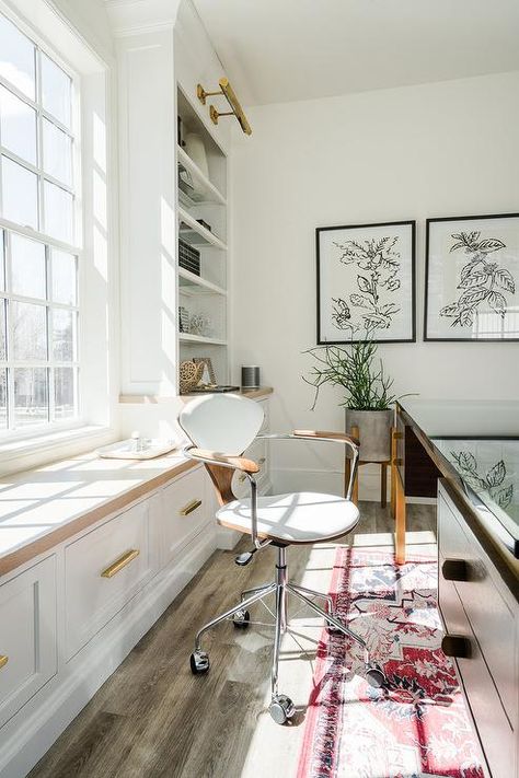 Well appointed home office features a wood top white window seat fitted with drawers donning brass hardware and positioned behind a Cherner Task Chair placed on a red vintage rug at a vintage desk. Desk With Window Behind, Zen Workspace, Bookshelf Lights, Home Office Vintage, Mediterranean Farmhouse, Desk Window, Office Bookshelf, Personal Workspace, Colorado House