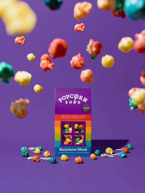 Commercial Product Photography For Popcorn Shed. Taking inspiration from the packaging's color scheme, we went for a purple backdrop which made the rainbow colored popcorn pop out even more. We added the textures of the popcorn to make it seem like a storm of colorful popcorn. #commercialphotography #productphotography Pop Color Photography, Summer Drink Ads Creative Advertising, Cereal Photoshoot Photo Ideas, Sweets Product Photography, Popcorn Product Photography, Packaging Photography Ideas, Candy Photography Food Styling, Packaged Food Product Photography, Candy Product Photography