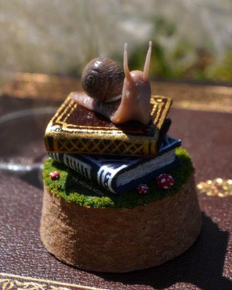 A lil something new for my spring collection!! Miniature snail sculpture jars! 🐌📚🍄 The snail and teeny tiny mushroom caps are hand sculpted with polymer clay. I made the books from recycled cardboard and secondhand leather scraps! They're hand painted with shimmery gold and silver inks and sealed with a glossy varnish. Everything is mounted on a mossy cork with my logo engraved into the bottom! One of these has already found a home (thank you so much!!!) but I do still have the other one l... Clay Snails, Polymer Clay Snail, Fairy Miniatures, Snail Sculpture, Mushroom Caps, Tiny Mushroom, Stuffed Mushroom Caps, Clay Inspiration, Recycled Cardboard