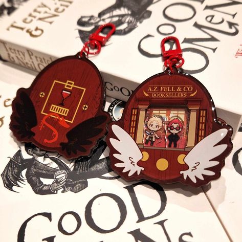 Good Omens-Book-A-Gotchi! Get ready to take your favourite Ineffable Husbands with you wherever you go with this Good Omens-inspired Tamagotchi-style shaker keychain! Inspired by the set of the TV show, the case depicts A. Z Fell & Co - Aziraphale's bookshop, with both Aziraphale and Crowley perfectly poised inside to take on an apocalypse or two, or three! With stunning pixel art by Naomi, this book-a-gotchi keychain makes a charming addition to any collection! Perfect for bookworms and fans of Good Omens Keychain, Good Omens Bookshop, Aziraphale's Bookshop, Good Omens Merch, Good Omens Pixel Art, Good Omens Crochet, Aziraphale And Crowley, Shaker Keychain, Old Married Couple