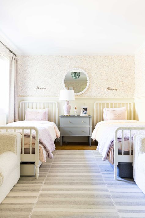 A girl's bedroom is her palace, ready to take on the world with style and comfort. This lovely girl's bedroom features two individual beds, a beautiful white and pink wall print, a round-shaped mirror, and a cute table lamp. Could it be any more charming Double Bed Girls Room, White And Pink Wall, Traditional House Decor, Pink Wall Print, Twin Girl Bedrooms, Girl Bedroom Ideas, Shared Girls Bedroom, Cute Table, Cama Individual