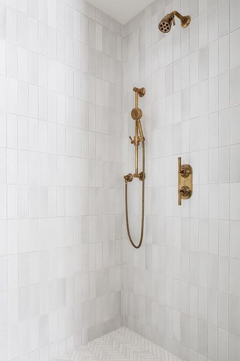 Shower features light gray glazed vertical stacked wall tiles, an aged brass shower kit and light gray marble herringbone shower floor tiles. Herringbone Shower Floor, Vertical Shower Tile, White Shower Tile, White Tile Shower, Kate Marker Interiors, Subway Tile Showers, Subway Tiles Bathroom, Shower Wall Tile, Marble Showers