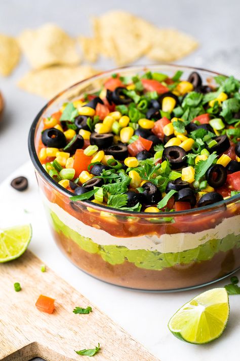 Vegan 7 Layer Dip Recipe layered with guacamole, beans, salsa, sour cream, corn, tomatoes and olives is a great centerpiece for everyone to gather around. Perfect snack for sport events, movie night or any casual get together with family and friends. Easy, healthy and ready in under 15 minutes. #veganrecipes #sevenlayerdip #healthyrecipes #healthybeandip #wfpb Vegan Layered Bean Dip, Layered Bean Dip Recipe, 7 Layer Bean Dip, 7 Layer Dip Recipe, Layered Bean Dip, Layered Dip Recipes, Whole Foods, Bean Dip Recipes, Seven Layer Dip