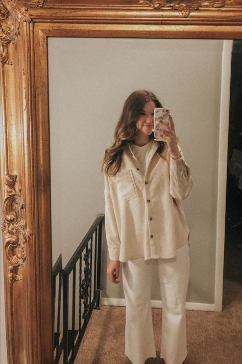 Carolynn is holding her phone and taking a mirror selfie through a gold ornate mirror mounted on the wall. She's wearing a cream corduroy jacket, white jeans, a white boxy t-shirt, Kate Spade gold initial necklace, and sweater booties White And Cream Outfits, Cream Corduroy Shacket Outfit, White Corduroy Shirt Outfit, Cream Corduroy Shirt Outfit, Cream Corduroy Jacket Outfit, White Corduroy Jacket Outfit, Cream Corduroy Pants Outfits, White Shacket Outfit, White Fall Outfit