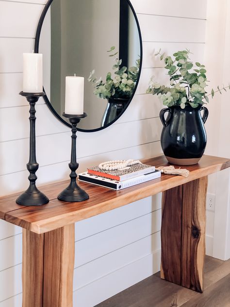 A simple yet elegant approach to a front entry table. The round mirror gives the modern farmhouse vibe, while the oversized pot, simple candlesticks and live edge wooden table allow for some class. Entry Table With Off Center Mirror, Entry Table Decor Simple, Modern Wood Entry Table, Wooden Entrance Table, Wood Entry Table Decor, Rustic Wooden Entry Table, Wooden Console Table Design Modern, Simple Foyer Ideas, Wooden Entryway Table