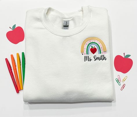 🍎Crafted with comfort in mind, our Teacher Rainbow Embroidered Sweatshirt features a soft and plush fabric that will keep you warm on chilly school days or cozy weekends. The classic crewneck design ensures a timeless and versatile look, making it easy to pair with your favorite jeans, leggings, or casual bottoms. Teacher Embroidered Shirt, Smiley Face Teacher Shirt, Embroidered Teacher Sweatshirt, Playful Cotton T-shirt For Back To School, White Crew Neck T-shirt For Teacher Appreciation, Casual Bottoms, Crewneck Design, Embroidered Crewneck, Personalized Teacher Gifts