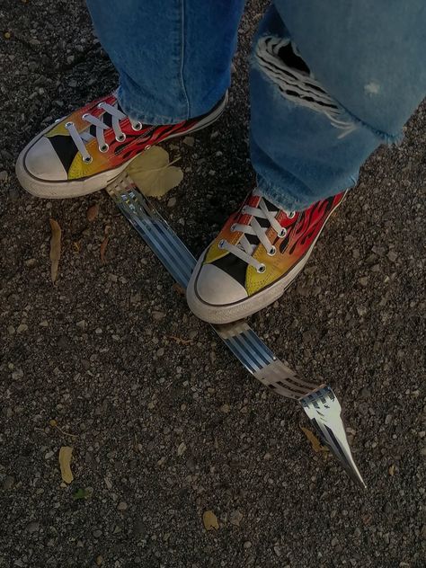 My friend riding a stick made of metal with an aesthetically pleasing gray colour, she is wearing a pair of high converse chuck taylor with an indie and vibrant flame print yellow, orange, and red. She is above an asphalt surface with some rock texture and leaves around her shoes. She is wearing light blue jeans with holes. Fire Converse, Converse Aesthetic, Shoes Cool, Print Shoes, Retro 70s, Aesthetic Grunge, Girls Life, Converse Chuck Taylor All Star, Fashion Aesthetic