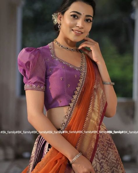 Do you need a beautiful and unique half saree for your next special occasion? Look no further than this lavender and orange Banarasi Silk lehenga! This gorgeous blouse features a collared V-neckline and puff sleeves with lace detailing on the yoke and sleeves, and the fabric used for it is golden tissue silk. The back of this dress is surely a head-to-turn pattern. It is paired with an organza silk-bordered dupatta. Whether you’re attending a wedding, a party, or a family occasion, this Banar... Organza Blouse Designs, Net Saree Blouse, Silk Half Saree, Lavender And Orange, Long Blouse Designs, New Saree Blouse Designs, Lehenga Designs Simple, New Blouse Designs, Blouse Designs Indian