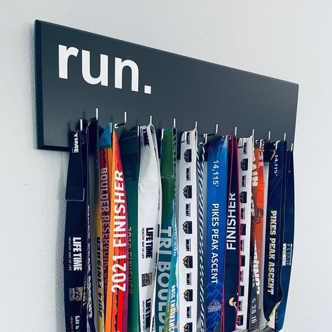 "Running Medal Holder, black with \"chrome\" \"run.\" vinyl, Large 23 1/2 \" x 7 1/2\" medal hanger with 11 or 21 hooks. Our run medal hangers are now available with 3D lettering in aluminium or acrylic, please check our listings for it! Details: - 11  or 21 nickel plated or white rubber coated hooks with \"shoulder\" . (Each hook can hold more than one medal.) - approx. 23.5 inches wide and 7.5 inches high. - Hand painted with 3 coats of paint. - Lettering and graphics are applied with vinyl. - Medal Hanger Ideas, Running Medal Display Ideas, Paint Lettering, Running Medal Holder, Medal Hangers, Running Medal, Black With Chrome, Athletics Track, Field Athletes