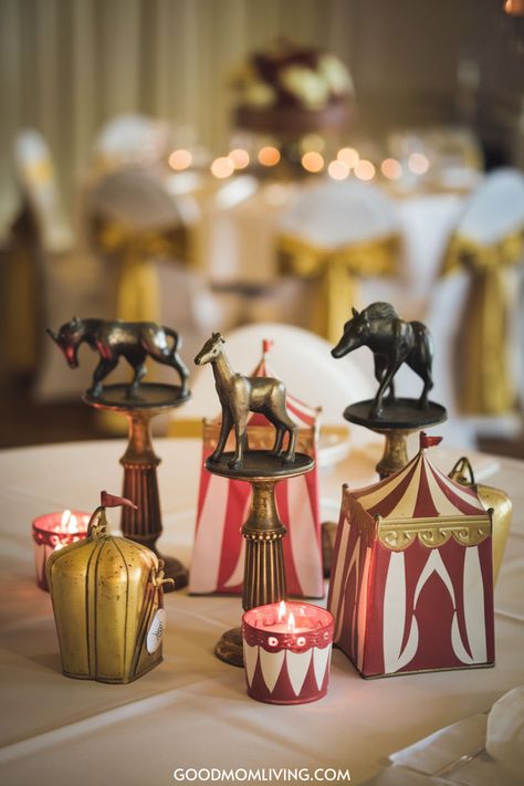 Decorative circus-themed table centerpiece featuring vintage animal figurines and red and white striped tents, set against a backdrop of elegantly draped chairs with golden sashes and soft candlelight. Vintage Carnival Birthday Party, Circus Theme Dinner Party, Carnival Home Decor, Big Top Circus Party, Circus Table Setting, Carnival Christmas Party Theme, Carnival Table Centerpieces, The Greatest Showman Theme, Circus Centerpieces Ideas