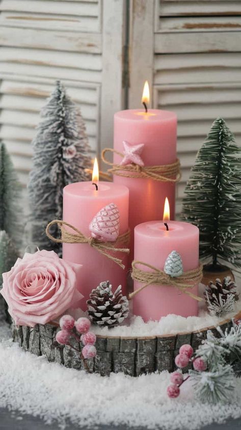 A beautiful and cozy winter-themed arrangement. At the center, there are three pink pillar candles of varying heights, each decorated with twine and delicate holiday ornaments such as pink and silver pinecone-shaped decorations and a small pink star ornament. The candles are lit, casting a warm, soft glow. Pink Christmas Table Centerpieces, Pink Christmas Candles, Desk Themes, Pink Christmas Table Setting, Pink Pillar Candles, Pink Shabby Chic Christmas, Christmas Tree Roses, Pink Christmas Table, Champagne Christmas Tree