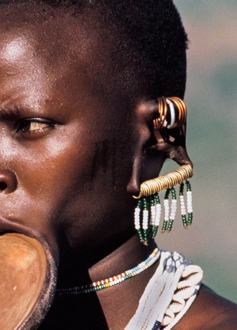 This image is from our book PAINTED BODIES
“A Surma bride from Ethiopia wears a clay lip plate inserted into her lower lip six months before marriage.This plate is worth seventy-five head of cattle. She also decorates her upper and lower ear lobes with brass and copper rings from which she hangs beaded tassels.“
Painted Bodies by Angela Fisher and Carol Beckwith is available on Amazon and many good bookstores. Erykah Badu Shaved Head, Zulu Head Beads, Erykah Badu Gold Teeth, Lower Lip, Copper Rings, Beaded Tassels, Ethiopia, Bookstore, Lips