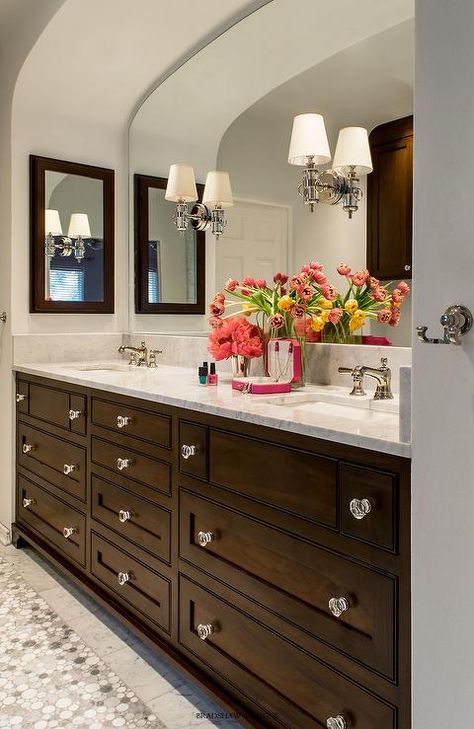 Chic bathroom boasts an arched alcove filled with a dark brown double washstand adorned with glass knobs topped with white marble fitted with his and hers sinks under an arched mirror lit by Thomas O'Brien Jonathan Sconces flanked by dark brown medicine cabinets. Arched Alcove, Dark Brown Bathroom, Bathroom Cabinet Knobs, Bathroom Dark, Dark Brown Cabinets, New Bathroom Ideas, Double Sinks, Brown Cabinets, Arched Mirror