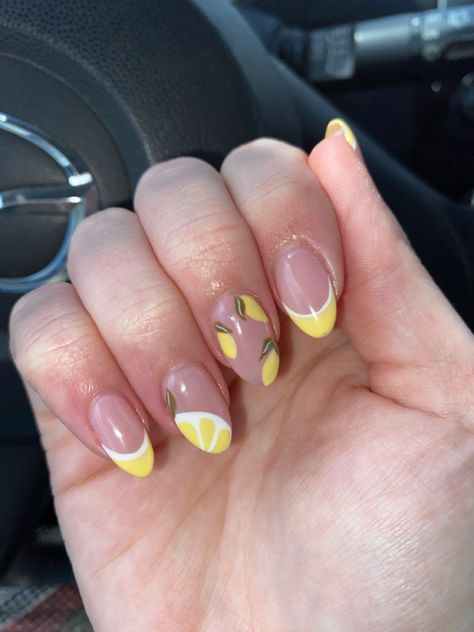 Hand bent to show off gel nails with yellow and white lined French tips, nude base, 3 little lemons with green stems on the middle finger and half a lemon with a green stem on the edge of the ring finger. Double heart ring on the middle finger in front of a steering wheel. Italian Nail Designs Style, Yellow And White French Tip Nails, Lemon Nails Designs, Yellow French Tip Nails, Yellow French Tips, Lemon Nail Art, Nails With Yellow, Nude Gel Nails, Yellow French Tip