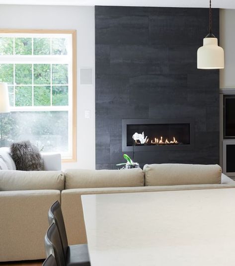 Living room with a fireplace with black large-format tile. Large Black Tile Fireplace, White Tiled Fireplace Ideas, Black Tile Fireplace, Tile Around Fireplace, Fireplace Chimney, Living Room With A Fireplace, Tiled Fireplace, Fireplace Tiles, Slate Fireplace