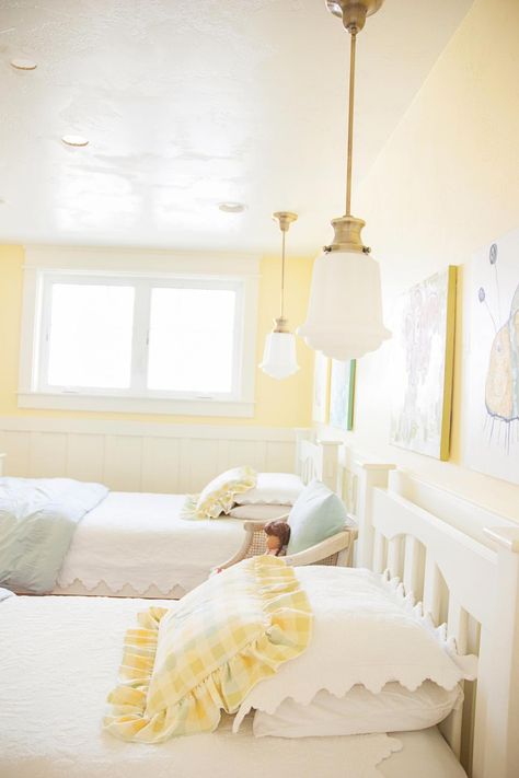 The beautiful color of yellow on the walls in this country-style bedroom is cheery enough for two young girls yet soft enough to grow with them. Pendant lights with individual switches hang above each bed, so the girls can choose to read at night. Light Yellow Bedrooms, Yellow Girls Room, White Girls Bedroom, Yellow Girls Bedroom, Yellow Bedroom Walls, Yellow Kids Rooms, Shared Girls Room, Country Style Bedroom, Big Girl Bedrooms