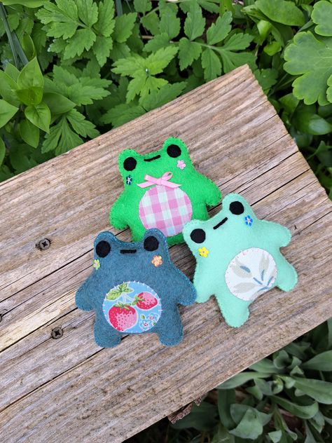 These little guys are ready to find a home. They're handmade from felt and fabric and full of personality. They're very hungry though and require a picnic immediately! Meet the frogs: Leaf - shy but loves to frolic in the leaves. (Light green leaf tummy) Pink - always well dressed and is usually in charge of directions (bright green pink check tummy) Strawb- zero thoughts unless its about food. Excited to find out what you're having for dinner (blue with strawberry tummy) *cat not included Felt Frog Keychain, Felt Fabric Crafts Ideas, Handmade Gift Ideas For Best Friend Diy, Easy Handmade Gifts For Friends, Felt Plushies Pattern, Little Sewing Projects, Frog Sewing, Felt Frog, Kawaii Embroidery