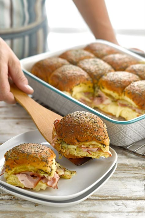 A person placing a ham and cheese slider roll on a plate with a wooden spatula on a table. Brioche Slider Buns Recipe, Ham And Cheese Brioche Sliders, Fancy Ham Sandwiches, Brioche Bun Sandwich Ideas, Brioche Buns Sandwiches, Brie Sliders, Brioche Sliders, Brioche Sandwich, Sandwich Melts