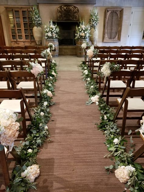 Sonoma Wedding Ramekins - Indoor wedding aisle floral featuring eucalyptus garland lining the aisle dotted with ivory and blush flowers. Chair bouquets, Altar flowers on wine barrels. #Ramekinswedding #Sonomawedding #aislefloral #winebarreltoppers Wedding Aisle Garland Decor, Eucalyptus Aisle Runner, Eucalyptus Lined Aisle, Aile Flowers Wedding, Wedding Aisle Eucalyptus, Wedding Aisle Indoor Decorations, Wedding Aisle Garland, Wedding Aisle Florals Indoor, Elegant Aisle Decorations Wedding