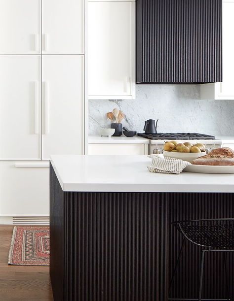 The peninsula and vent hood were clad in reeded oak that’s stained in a rich ebony tone, while the rest of the cabinets were lacquered in a crisp white, their outlines subtly defined by pencil-trim molding. | Photographer: Donna Griffith | Designer: Jordy Fagan & Alana Firestone, Collective Studio Fluted Island, Fluted Kitchen, White Stone Backsplash, White Marble Backsplash, Kitchen Hood Ideas, Kitchen Hood Design, Collective Studio, Sleek Cabinet, Herringbone Wood Floor