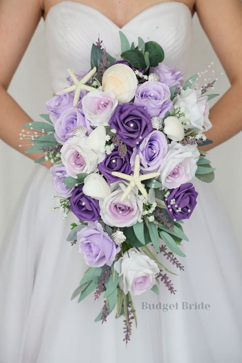 This lovely assortment of lavender, wisteria and wisteria centered roses is bound to turn heads on your wedding day. This lovely cascading brides’ bouquet from the is an absolutely breathtaking arrangement for any bride to be, in any season. Sage greenery and starfish and pearls complete the look and add a delicate realism to this beautiful bouquet. This bouquet is 10” wide, 18” long, and is crafted by our in-house florists without using a foam base to anchor the flowers to the bouquet. Instead, Wedding Cake Light Purple, Fake Wedding Flowers, Small Bridesmaid Bouquets, Fresh Wedding Flowers, Purple Bridal Bouquet, Budget Bride, Red Bouquet Wedding, Cascade Bouquet, Small Intimate Wedding