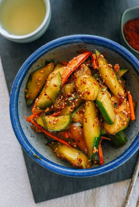 Bowl of spicy cucumber salad with flecks of chili flake and sesame seeds and a little sliced carrot in a blow-rimmed bowl with a cup of green tea in the corner Spicy Korean Cucumber, Oi Muchim, Banchan Recipe, Meal Starters, Meal Salads, Korean Cucumber Salad, Korean Cucumber, Woks Of Life, The Woks Of Life