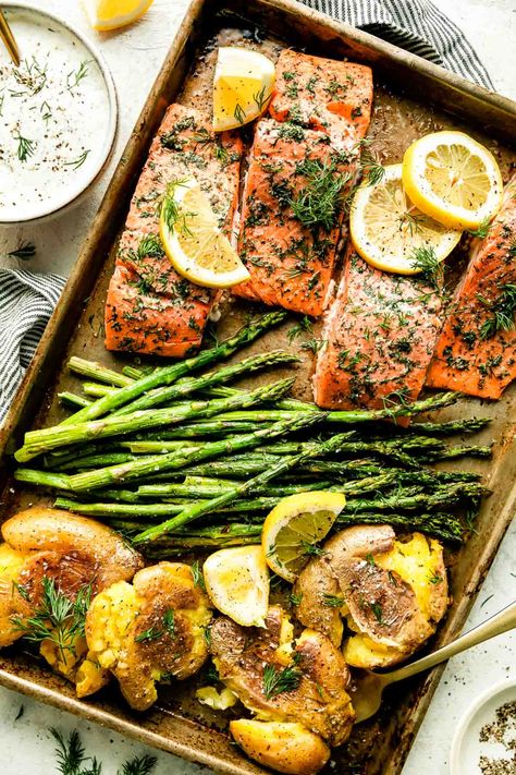 This Sheet Pan Salmon and Asparagus with Crispy Smashed Potatoes is an easy all-in-one dinner, perfect for springtime! Salmon fillets, seasoned with lemon & dill, bake on a sheet pan with asparagus spears until perfectly tender & flaky. Serve with crispy smashed potatoes (oven-roasted alongside the salmon!) & dill yogurt sauce to bring all the flavors together. A fresh & healthy weeknight dinner! #salmonandasparagus #salmonandpotatoes #sheetpansalmon #bakedsalmon #salmonrecipes #easydinnerideas Salmon Sheet Pan Dinner, Clean Eating Salmon, Dill Yogurt Sauce, Salmon Potatoes, Potatoes Oven, Salmon Dill, Baked Salmon And Asparagus, Sheet Pan Salmon, Salmon Asparagus