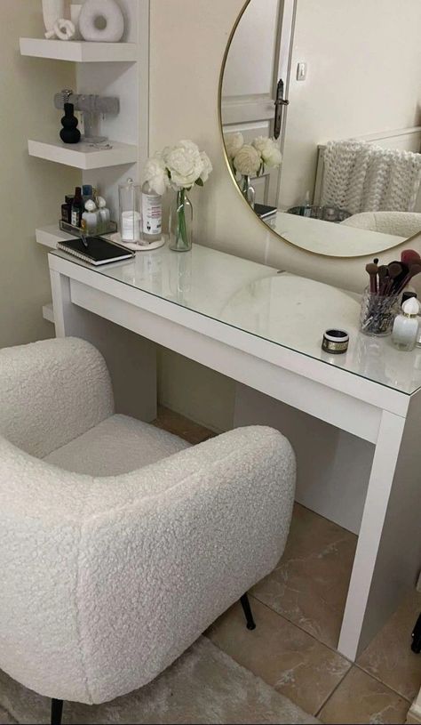 A modern, classy white vanity desk area. A nicely decorated tall shelf is located next to it, a gold-framed round mirror is above it and a few vases, flowers, makeup brushes, perfumes are set on it. White Glam Bedroom, Home Decor Ideas Minimalist, Makeup Vanity Chair, Room Decor Ideas Bedroom, Minimalist Living Room Apartment, Ideas For Small Bedrooms, Decor Ideas For Bedroom, Condo Living Room, Upholstered Bedroom