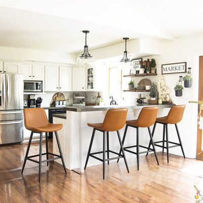 These counter stools bring a modern industrial vibe to your kitchen island or bar area. They arrive in a set of four, and they're crafted with an iron frame and splayed legs in your choice of neutral finish. The bucket-style seat with low backrests are wrapped in foam-filled faux leather upholstery for lots of cushioned support while you enjoy meals and conversation with friends and family. We also love how the wraparound footrests keep your feet cozy, too. Plus, the plastic glides on the legs h Modern Bar Stools Kitchen, Brown Stool, Island Bar Stools, Counter Stools With Backs, Brown Bar Stools, Leather Kitchen, Bar Stools Kitchen Island, Leather Counter Stools, Stools For Kitchen Island