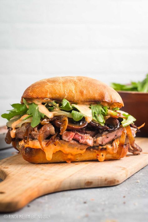 This grilled ribeye steak sandwich is loaded with roasted red pepper garlic aioli, arugula, provolone, caramelized onions, and mushrooms, all on a toasty ciabatta roll. You can even use thinly sliced leftover steak in this recipe! This sandwich is a great main course dish, and the sauce is out of this world! Steak And Pepper Sandwiches, Open Face Steak Sandwich, Sandwich Recipes With Arugula, Hot Dinner Sandwiches, Bistro Recipes Dinners, Best Steak Sandwich Recipe, Leftover Steak Sandwich, Italian Steak Sandwich, Sandwich With Arugula