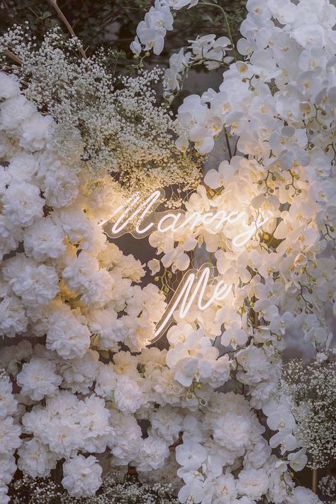 A romantic setting featuring a lush flower decor backdrop with a warm 'Marry Me' LED sign. Make your proposal remarkably heartwarming and eternally cherished. 💍🌸💡Pop the question surrounded by romance & warmth with our stunning flower decor & ‘Marry Me’ LED sign. Let love bloom as you create a moment that will be treasured forever. 💍🌹✨ Will You Marry Me Flower Wall, Floral Proposal Set Up, Will You Marry Me Sign Flowers, Marry Me Candles Proposal, Proposal Signs Marry Me Diy, Proposal Candles, Wedding Rental, Rental Business, Romantic Proposal