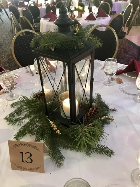 One of four centerpieces I made for my Michigan Winter Wedding! Candle, lantern, greenery, pine cone, gold accent. Follow me at __hannahhisey on instagram for more details on my winter wedding! Winter Wedding Lanterns, Winter Wedding Lantern Centerpieces, December Wedding Decor Ideas, Pine Greenery Wedding, Winter Lantern Centerpieces, Winter Wedding With Christmas Trees, Pine Cone Wedding Centerpieces, Evergreen And Gold Wedding, Evergreen Wedding Decor