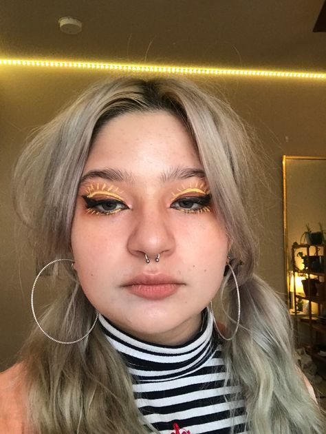 girl with yellow sun graphic eyeliner, in a striped turtleneck and an orange open short sleeve button up shirt and hoop earrings Yellow Liner Makeup Looks, Gen Z Eyeliner, Sun Eye Makeup, Sun Eyeliner, Yellow Graphic Liner, Sixties Makeup, Sunshine Makeup, Yellow Eyeliner, Starchild Tarot