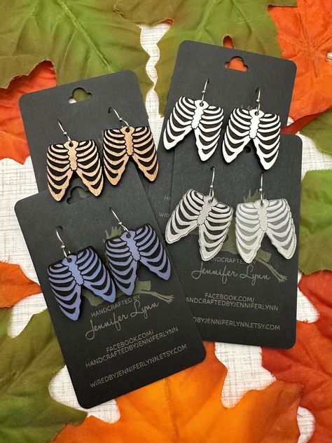 These boney rib cage earrings are laser engraved from either acrylic or maple ply. The result is a pair of spooky-fun earrings that are perfect for Halloween and all spooky season long!  OPTIONS INCLUDE:  - CHERRY WOOD - Laser cut from a piece of cherry ply, the engraved area is painted with a matte black that adds a distressed look to the wood.  - WHITE - Cut from a piece of white eucalyptus board. The white is slightly textured and the engraved portion is a dark brown. The backside of the earr Halloween Laser Ideas, Laser Halloween Ideas, Unique Laser Cut Ideas, Xtool S1 Project Ideas, Halloween Laser Projects, Laser Cut Projects, Laser Cut Halloween, Laser Earrings, Laser Jewelry