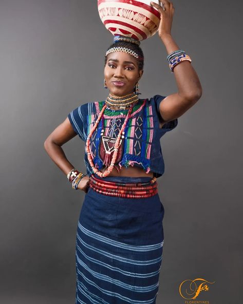 It is a picture of a Fulani Maiden wearing the traditional  blue stripped crop top and wrapper. The model is wearing an array of colourful beads on her head,neck and waist.
On top of her head is a Calabash.
The entire outfit can be rented for photo and film shoots. Fulani Traditional Attire, Fulani Clothing, Fulani Dress Styles, Hausa Bride, Nigerian Traditional Dresses, Traditional Wedding Attire, Dress Aesthetic, Nigerian Styles, Traditional Attire