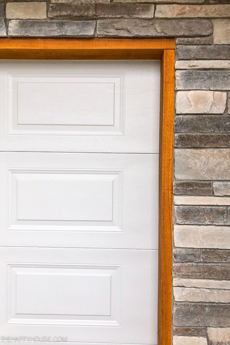 A white garage door, cedar trim and stone work. Cedar Trim Around Garage Door, Wood Trim Around Garage Door, Wood Trim Garage Door, White Garage Doors With Black Trim, Cedar Door Trim, Garage Trim Ideas Exterior, White House Cedar Accents, Cedar Trim Exterior, Garage Door Trim Ideas