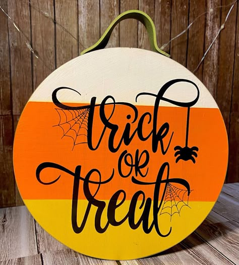 Trick or Treat! This cute little wood sign is perfect to add to your Halloween décor this year! It is so versatile because of its size. You can hang it by the olive green color leather strap at the top or it is thick enough that it will stand on its own! Would be perfect addition to put next to other décor or super cute all by itself.  The colors are painted to look like a candy corn candy; white, orange & yellow with the sides and back done in black and the vinyl lettering done in a black. Halloween Round Wood Signs Cricut, Cricut Round Wood Signs Halloween, Cricut Circle Wood Projects, Candy Corn Sign, Halloween Wood Rounds, Candy Corn Door Hanger, Round Halloween Signs, Fall Football Crafts, Halloween Round Wood Signs