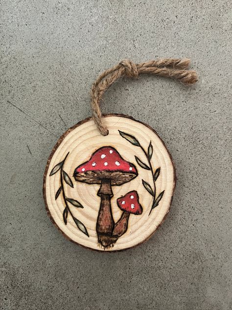 "This fun design is a spruce tree round with  mushrooms and leaves wood burned into it, painted with some colored pencil as well! It measures approximately 3.5\" x 3.25\" and already includes a twine hanging cord. Perfect for hanging on your wall, using as an ornament an much more! I have many other items you may be interested in so please check out my page!" Wood Burning Painting, Wood Burn Ornaments Tree Slices, Wood Burning Mushrooms, Fall Wood Burning Ideas, Painted Wood Rounds, Wood Burning Art For Beginners, Mushroom Wood Burning, Wood Burning Ornaments, Craft Fair Ideas To Sell