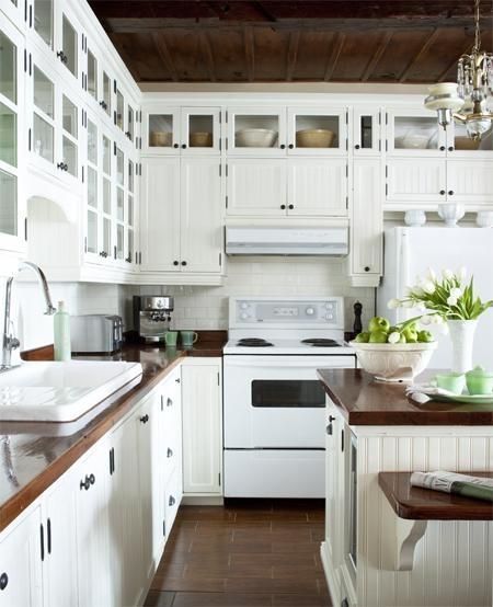 Stunning white kitchen design with off-white beadboard kitchen cabinets, glass-front cabinets, white subway tiles backsplash, butcher block countertops, white appliances and kitchen island. by Susan Butcher Block Countertops White Appliances, White Kitchen Cabinets With Butcher Block, Nice Kitchens, Kitchen Restoration, White Kitchen Appliances, Block Countertops, Bungalow Kitchen, Butcher Block Kitchen, White Tile Backsplash