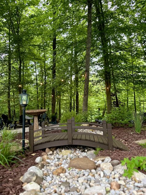 Dry creek bed in garden surrounding fire pit area. MY 2024 Small Bridge In Garden, Bed In Garden, Dry Creek Bed Landscape, Stream Landscaping, Creek Ideas, Landscape Island, Dry Stream, Ground Level Deck, Wooded Landscape