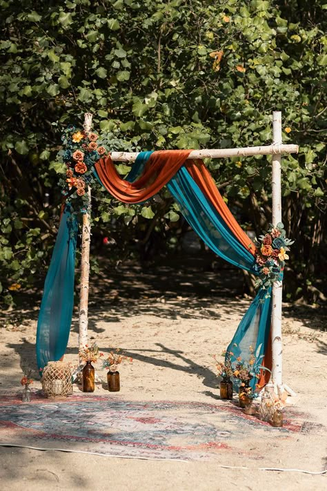 Wander through the forest with Ling’s Dark Teal & Burnt Orange collection. This rich palette combines warm and cool shades to create a rustic look ideal for autumn weddings. Adorn your bridal party with unique bouquets, corsages, and boutonnieres. Transform your venue with premade ceremony and reception decor. Or c Fall Wedding Backdrops Altars, Outside Arch For Wedding, Wedding Colors Teal And Orange, Teal And Burnt Orange Wedding Arch, Real And Burnt Orange Wedding, Dark Teal Orange Wedding, Western Wedding Seating Ideas, Teal Orange Red Wedding, Dusty Rose Burnt Orange Wedding