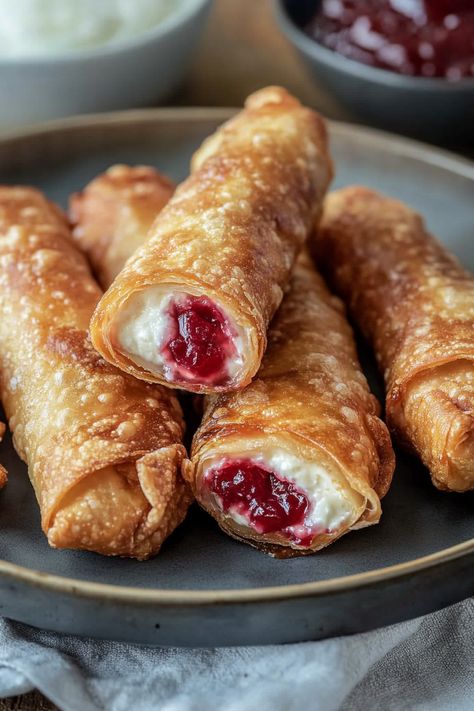 Cherry Cheesecake Egg Rolls offer a delightful twist on the traditional Asian appetizer! Packed with a tart cherry filling and luscious cream cheese, these crispy treats are easy to prepare and can be pan-fried, air-fried, or baked. Wrapped in wonton skins and sprinkled with cinnamon sugar, these dessert egg rolls are a quick and delightful Cheesecake Wontons Air Fryer, Crispy Cherry Cheesecake Egg Rolls, Cherry Cheesecake Rolls, Cherry Cream Cheese Egg Rolls, Desert Eggroll Recipe, Cherry Egg Rolls, Wonton Deserts, Sweet Egg Rolls Desserts, Air Fryer Cherry Cheesecake Egg Rolls