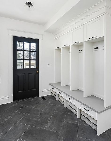 A black doors finished with nine glass panels opens to a white and gray mudroom boasting dark gray herringbone pattern floor tiles fixed beneath woven two-tone baskets. Bathroom Dark Grey Floor, Floor Herringbone Pattern, Gray Mudroom, Dark Grey Floor, Floor Herringbone, Tiles Herringbone, Bathroom Dark, Floor Tiles Design, Mudroom Flooring