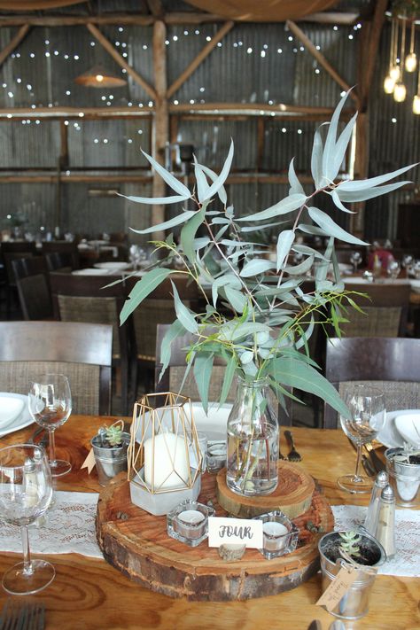 Simple wedding table centerpiece using Eucalyptus and wood rounds Easy Round Table Centerpieces, Eucalyptus Round Table, Wood Round Centerpiece With Eucalyptus, Wood Circle Centerpiece Wedding, Wood Round Centerpiece, Eucalyptus Centerpiece Round Table, Timber Rounds Wedding, Simple Wedding Centerpieces Wood Slice, Simple Wedding Table Centerpieces