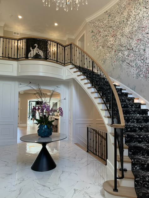 Who knew an entryway could be this stunning? This curved grand staircase truly makes a statement upon entering this home. No details were left untouched, from the floral mural on the wall, to the luxurious marble floor and box trim on the wall, this space is truly magical!   New Construction | Home Trends 2024 | Home Design | Minnesota Home Trends Small Grand Staircase, Trim On The Wall, Grand Entryway Foyers, Curved Staircase Foyer, House Flipper Ideas, Stunning Staircases, Staircases Ideas, Foyer Interior, Landed House